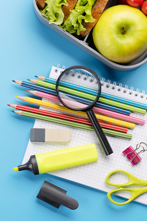 3B-lunchbox with a sandwich and fruit and school supplies on table.png