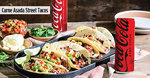 Carne asada street tacos on a plate with Coca-Cola and additional toppings on the side